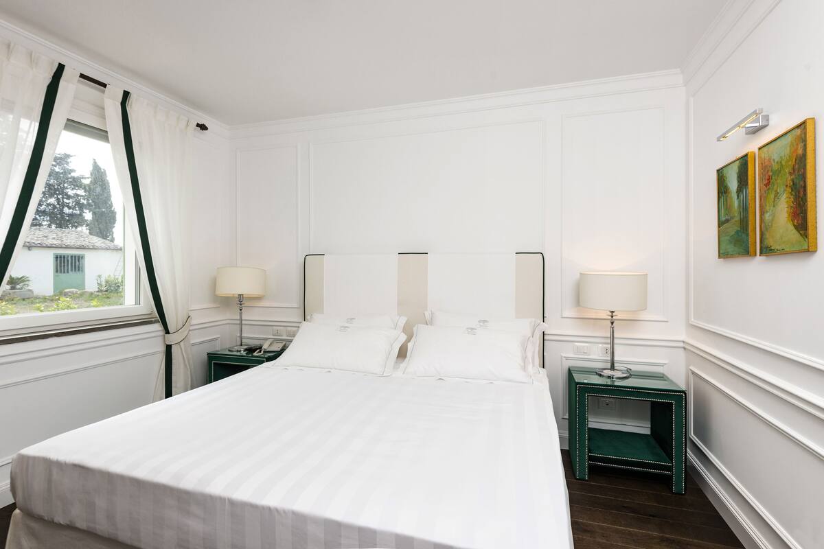 A neatly arranged hotel room with a large bed, two bedside tables, and a window with curtains.