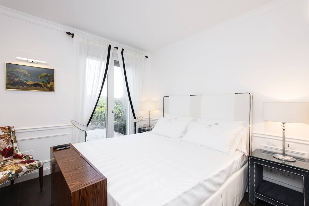A bedroom with a large bed, a nightstand, a chair, and a window with curtains.