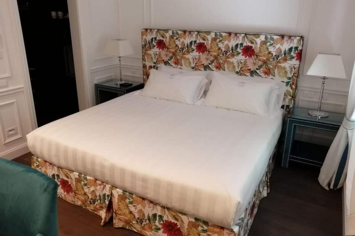 A neatly made bed with a floral headboard, two bedside tables with lamps, and a green chair.
