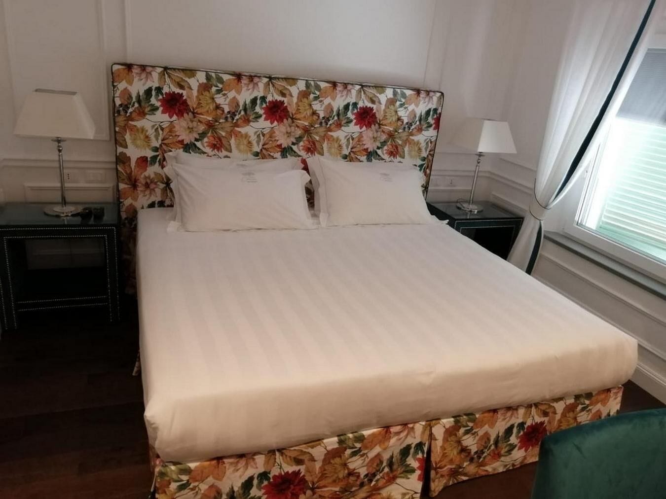 A neatly made bed with a floral headboard and white linens in a hotel room.