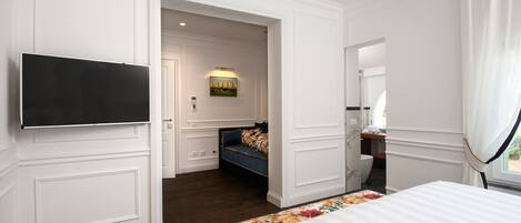 Habitación de hotel con una cama grande, un televisor montado en la pared, una zona de estar con un sofá y un sillón, y una mesita.