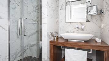 A modern bathroom with a glass shower enclosure, a wooden vanity with a white sink, and marble walls.