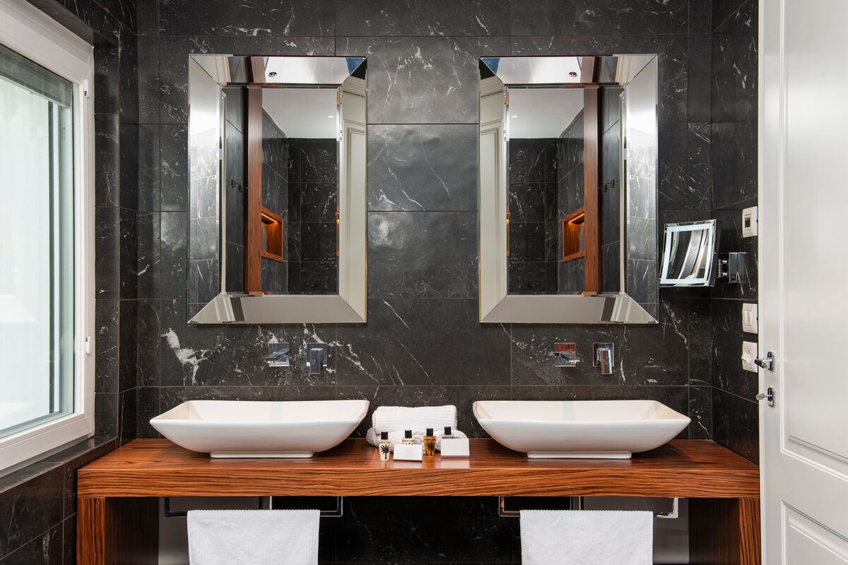 A modern bathroom with two large white sinks, dark marble walls, and a wooden vanity.