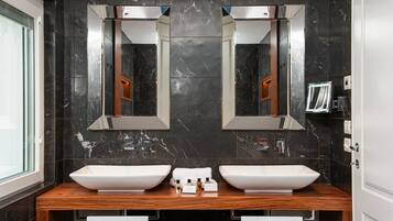 A modern bathroom with two large white sinks, dark marble walls, and a wooden vanity.