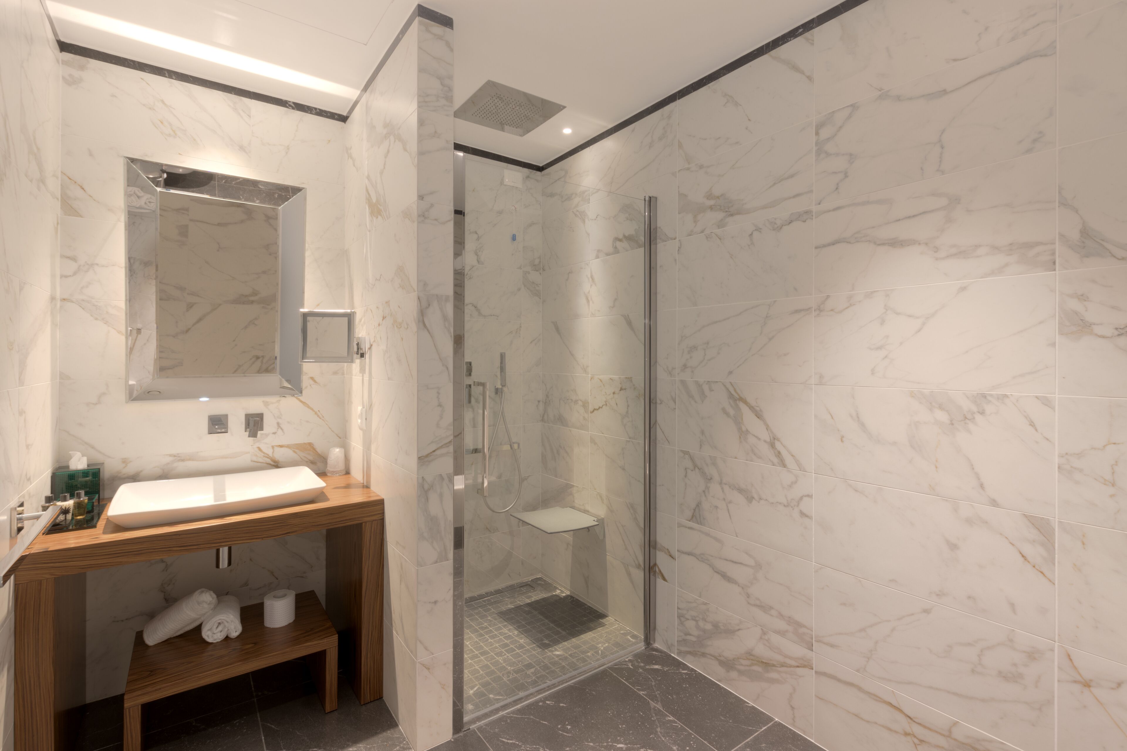 A modern bathroom with a marble sink, a glass shower enclosure, and a wooden vanity.