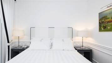 Habitación de hotel con una cama grande, dos mesitas de noche con lámparas, un cuadro en la pared y una ventana con cortinas.