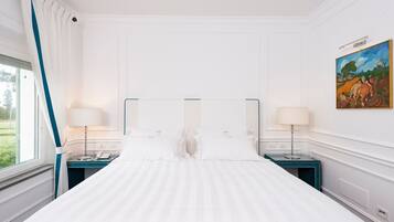 A hotel room with a large bed, two bedside tables, a window with curtains, and a painting on the wall.