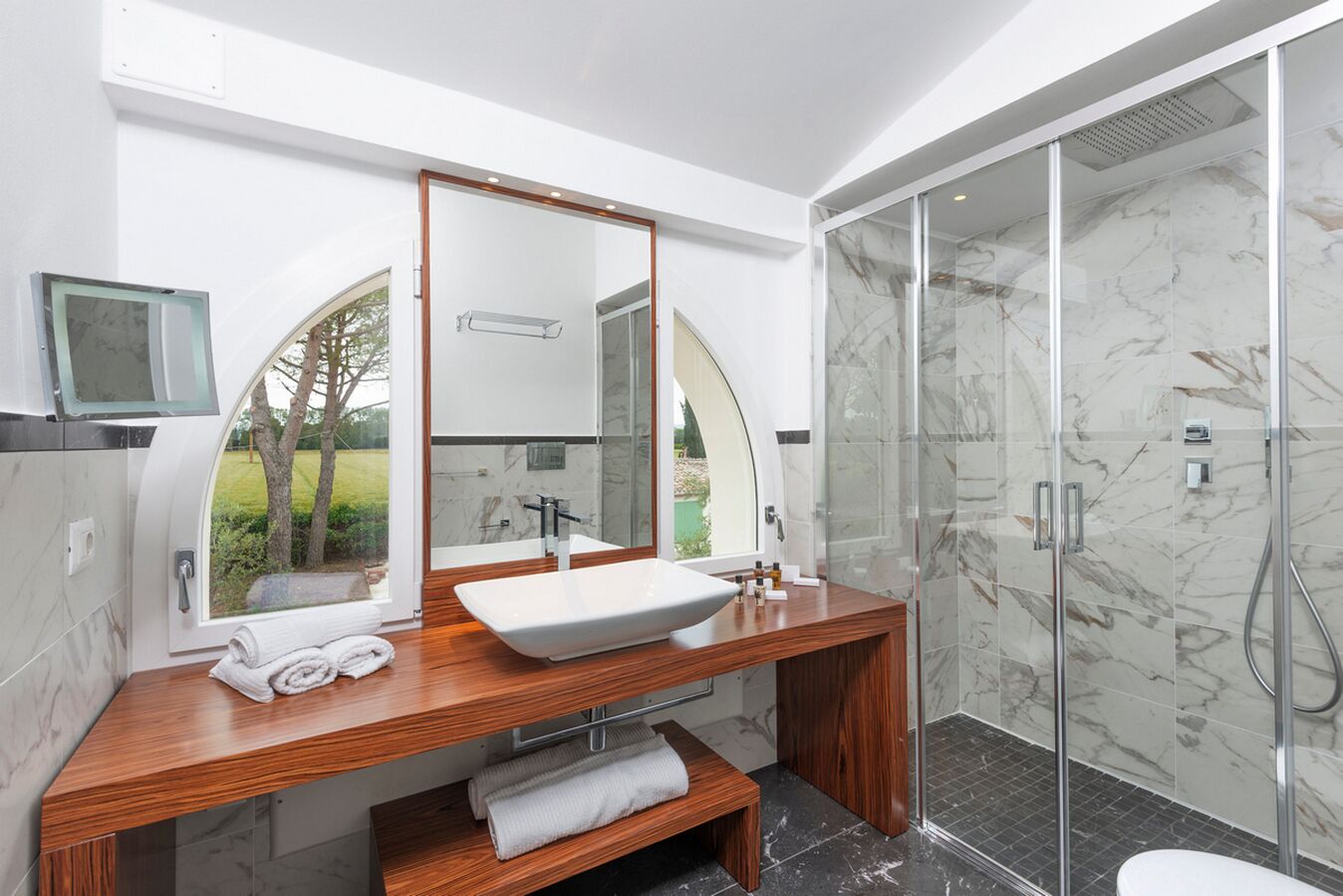 A modern bathroom with a large mirror, a wooden vanity, a freestanding bathtub, and a glass-enclosed shower area.