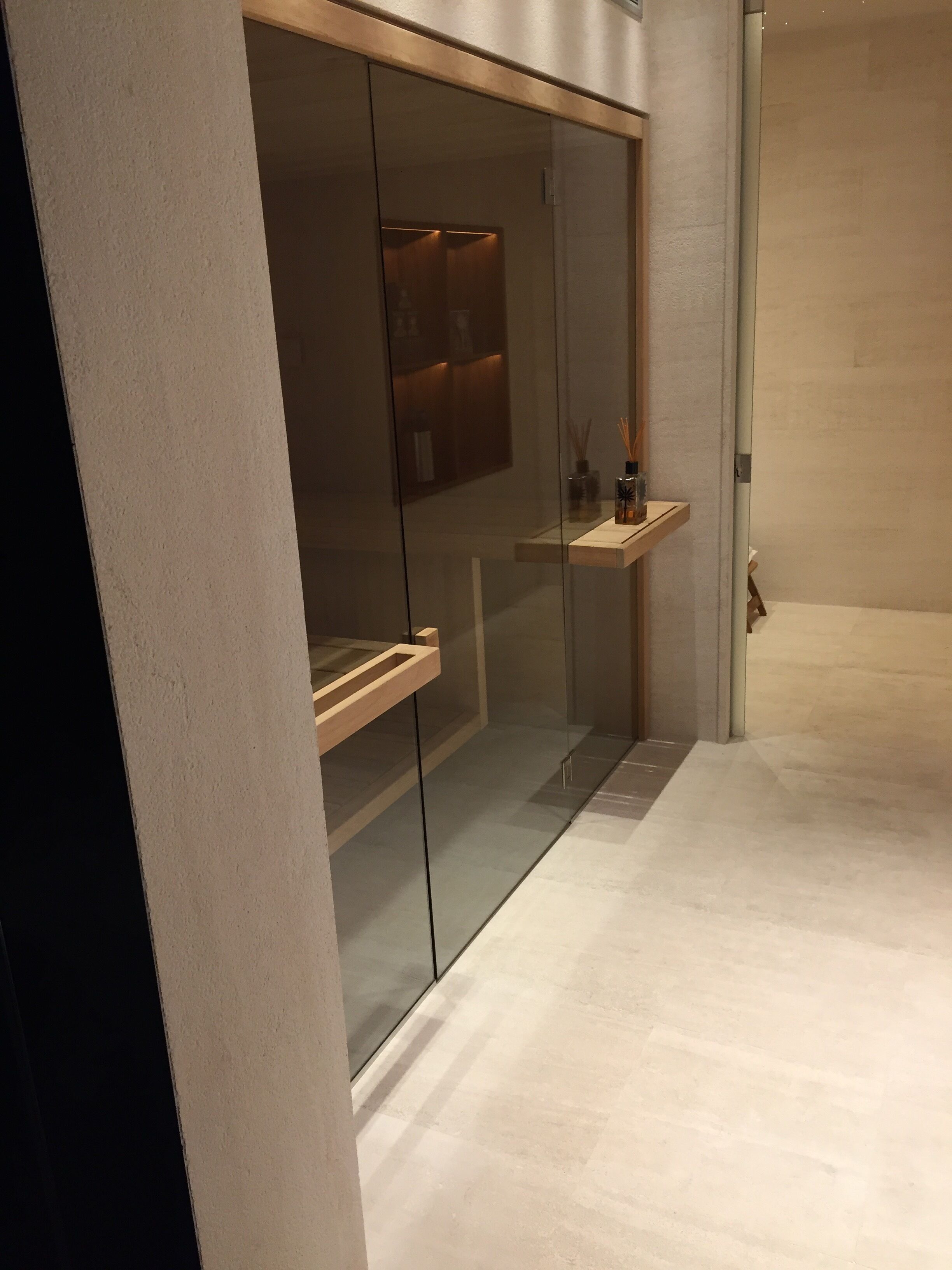 Ein modernes Interieur mit Glastrennwand, Holzregal und Fliesenboden.