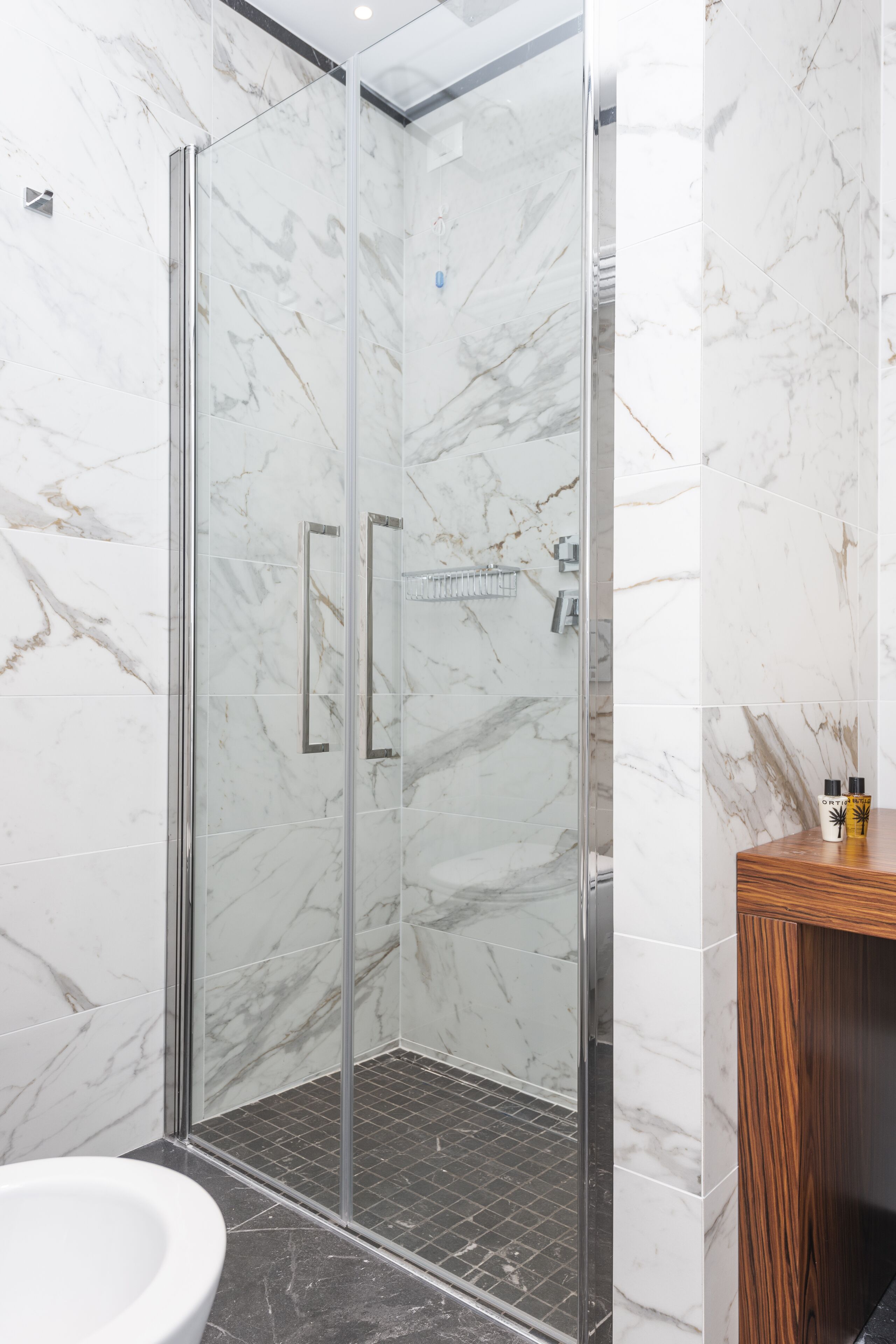 A modern bathroom with a glass-enclosed shower, marble walls, a wooden vanity, and a white sink.