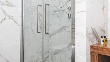 A modern bathroom with a glass-enclosed shower, marble walls, a wooden vanity, and a white sink.