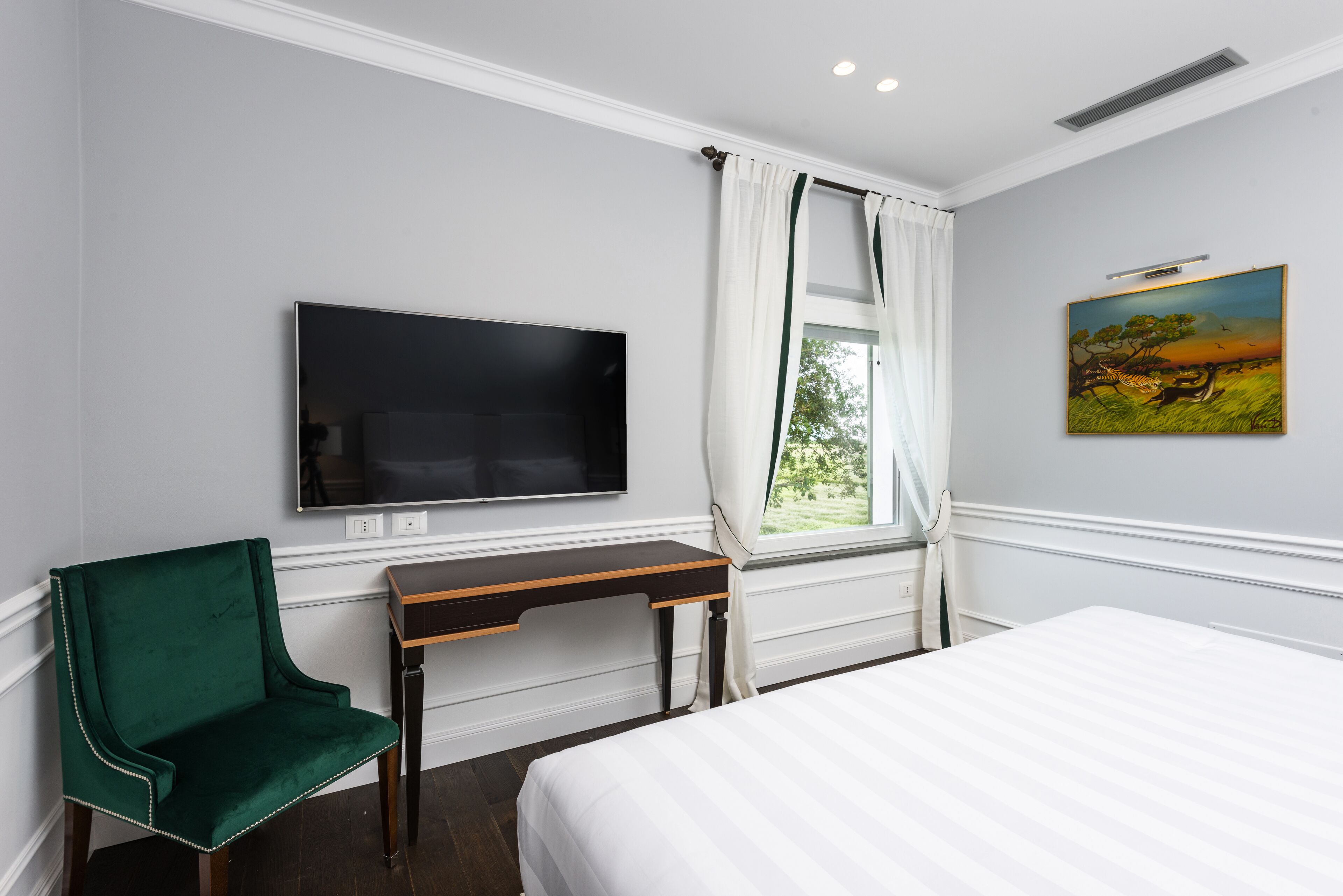 A hotel room with a bed, a desk, a chair, a TV, and a window with curtains.