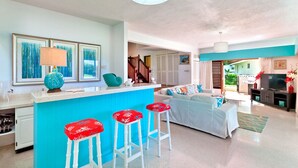 Een lichte woonkamer met een blauwe accentmuur, een witte bank en rode barkrukken.