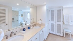 A modern bathroom with two sinks, a large mirror, and a walk-in shower.