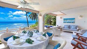 A dining area with a view of the ocean, wicker furniture, and a painting on the wall.
