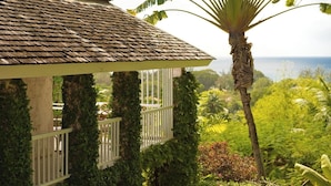 A house with a tiled roof and a balcony with white railings, surrounded by lush greenery and a view of the ocean. - 17th Century Sugar Mill Near Beach - Mullins Mill (Mullins)