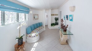 Una habitación luminosa y bien iluminada con un banco curvo blanco, una mesa de centro de cristal y una escultura de piedra sobre un pedestal.