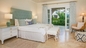 A bedroom with a large bed, two bedside tables, a bench, and a chair. There is a balcony with curtains and a view of greenery. - Beachfront Caribbean Elegance - Schooner Bay 205 (1 bed) (Speightstown)