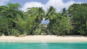 A beach with clear turquoise water, palm trees, and a gazebo-like structure surrounded by lush greenery.