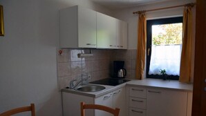 A compact kitchen with a sink, stove, and cabinets. There is a window with curtains and a small plant on the windowsill. - Apartment Lenardic Bled (Bled)