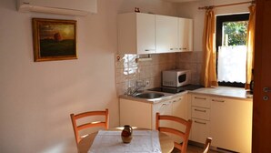 A compact kitchen with white cabinets, a microwave, a sink, and a dining table with chairs. - Apartment Lenardic Bled (Bled)