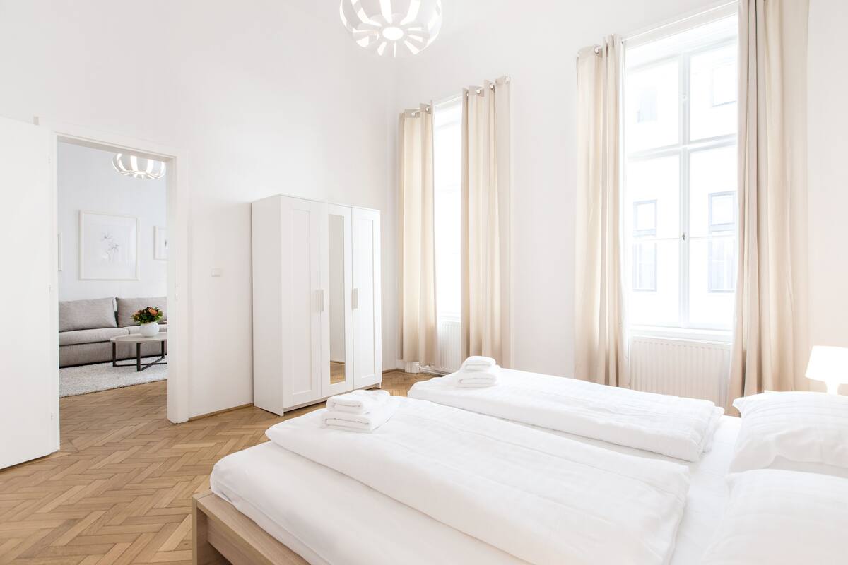 Moderni hotellihuone, jossa on kaksi sänkyä, vaatekaappi, sohva ja näkymä kaupunkiin.