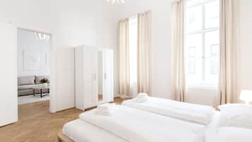 A modern hotel room with two beds, a wardrobe, a sofa, and a view of the city.