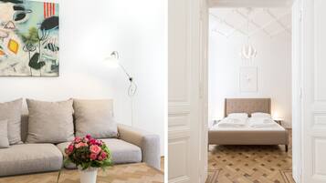 Un soggiorno moderno con un divano, una lampada da terra e un quadro. Si vede anche una camera da letto con un letto, un comodino e un lampadario.