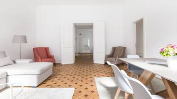 Ein modernes Wohnzimmer mit Holzboden, einem weißen Sofa, einem roten Sessel und einem Essbereich mit weißem Tisch und Stühlen.