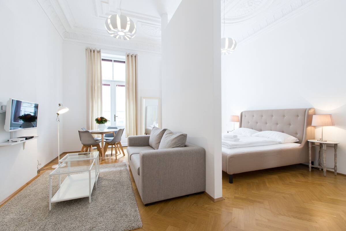 Moderni hotellihuone, jossa on sohva, sänky, televisio, ruokapöytä ja kattokruunu.
