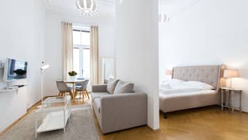 A modern hotel room with a sofa, a bed, a TV, a dining table, and a chandelier.