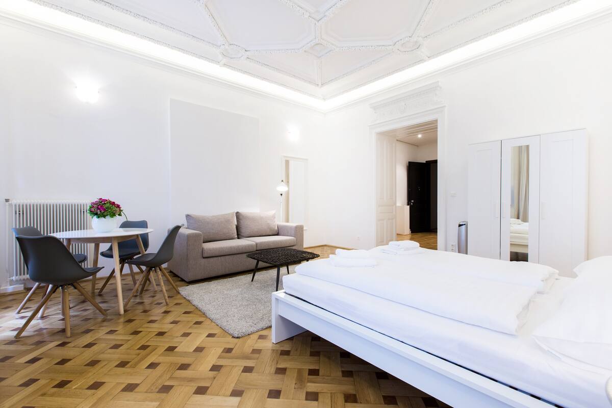 Moderni hotellihuone, jossa on sänky, sohva, ruokapöytä ja pieni keittiöalue.