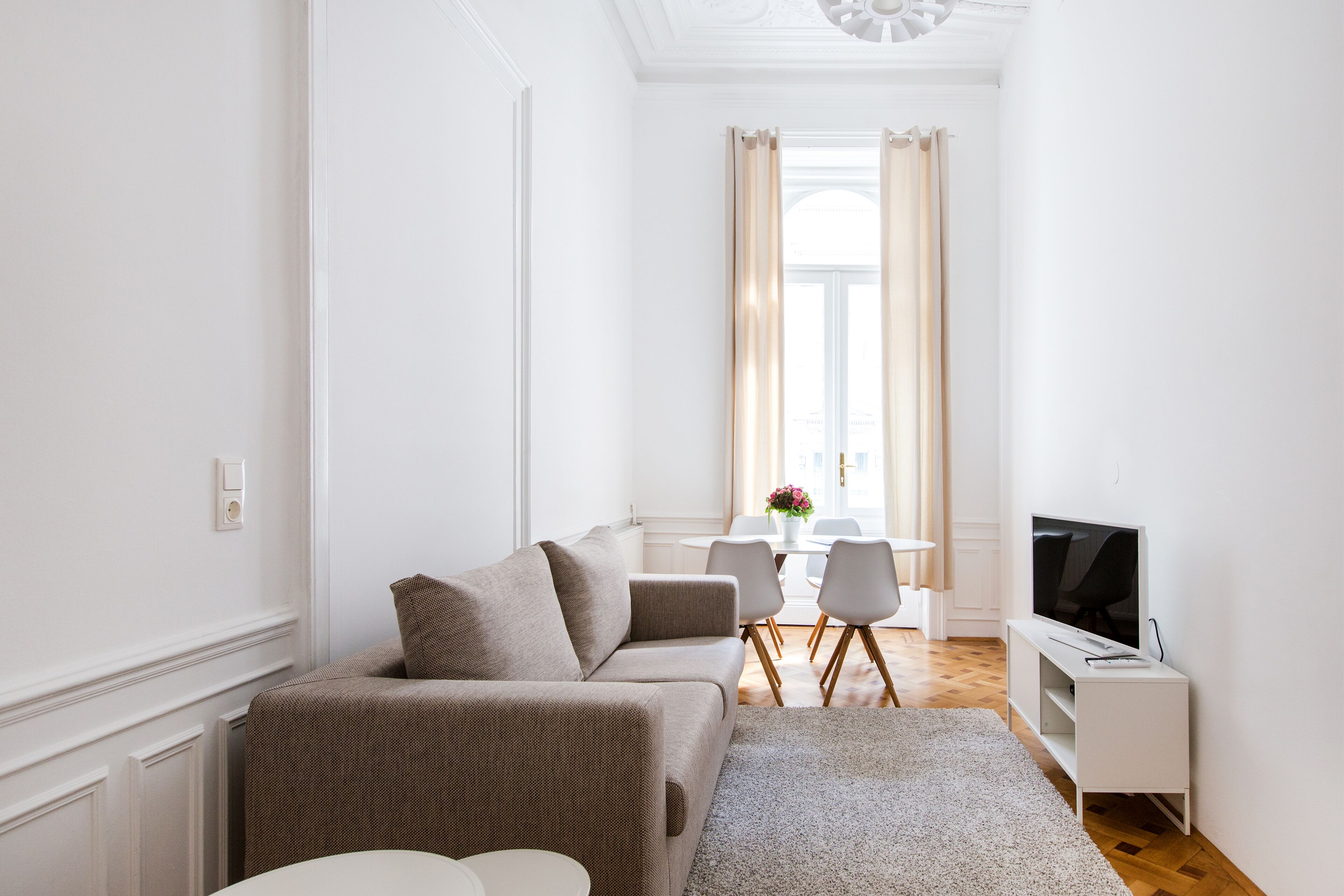 A modern living room with a sofa, a TV, and a dining area in the background.