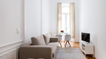 A modern living room with a sofa, a TV, and a dining area in the background.