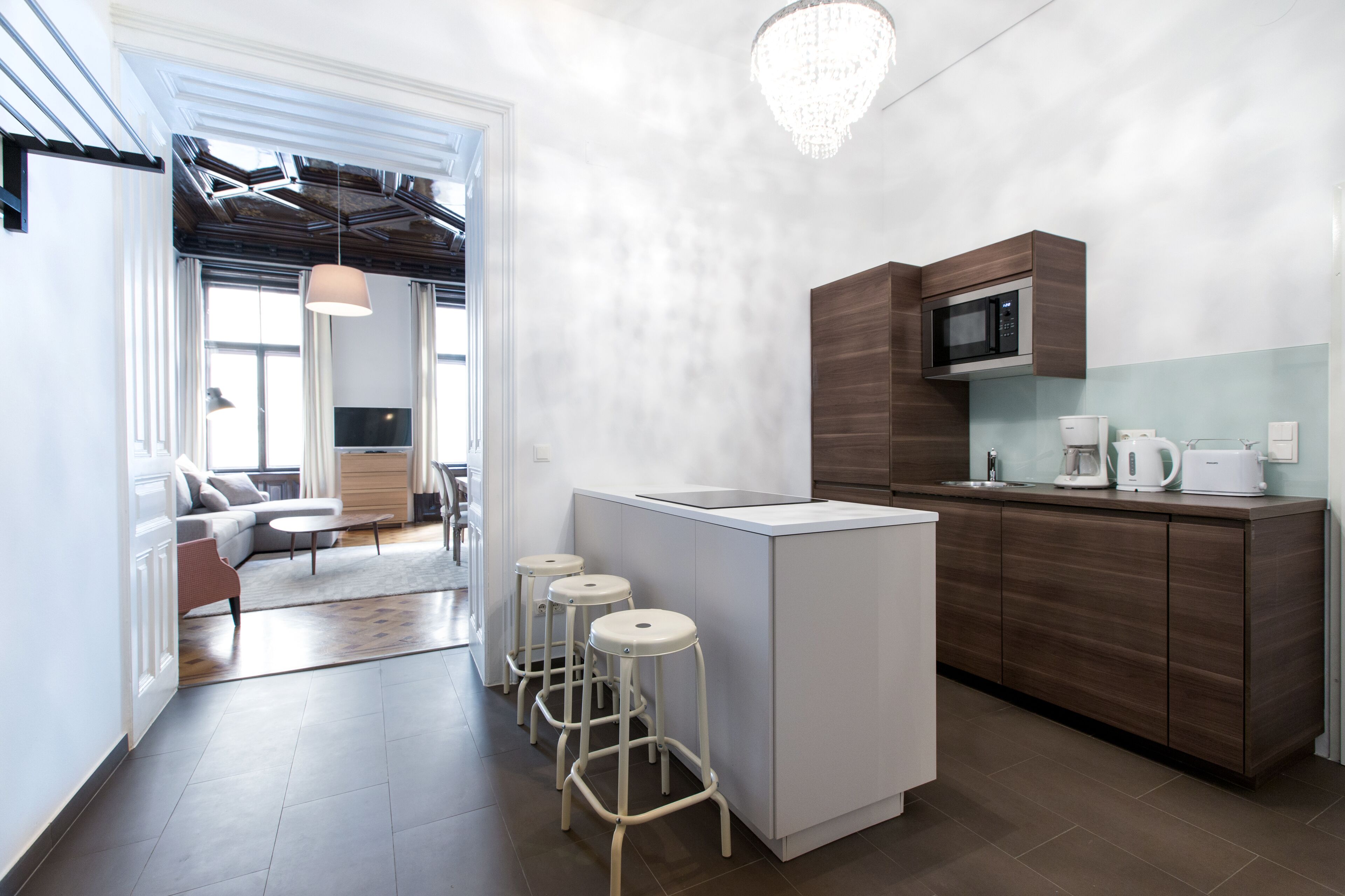 A modern kitchen with a central island, bar stools, a microwave, and a coffee machine.