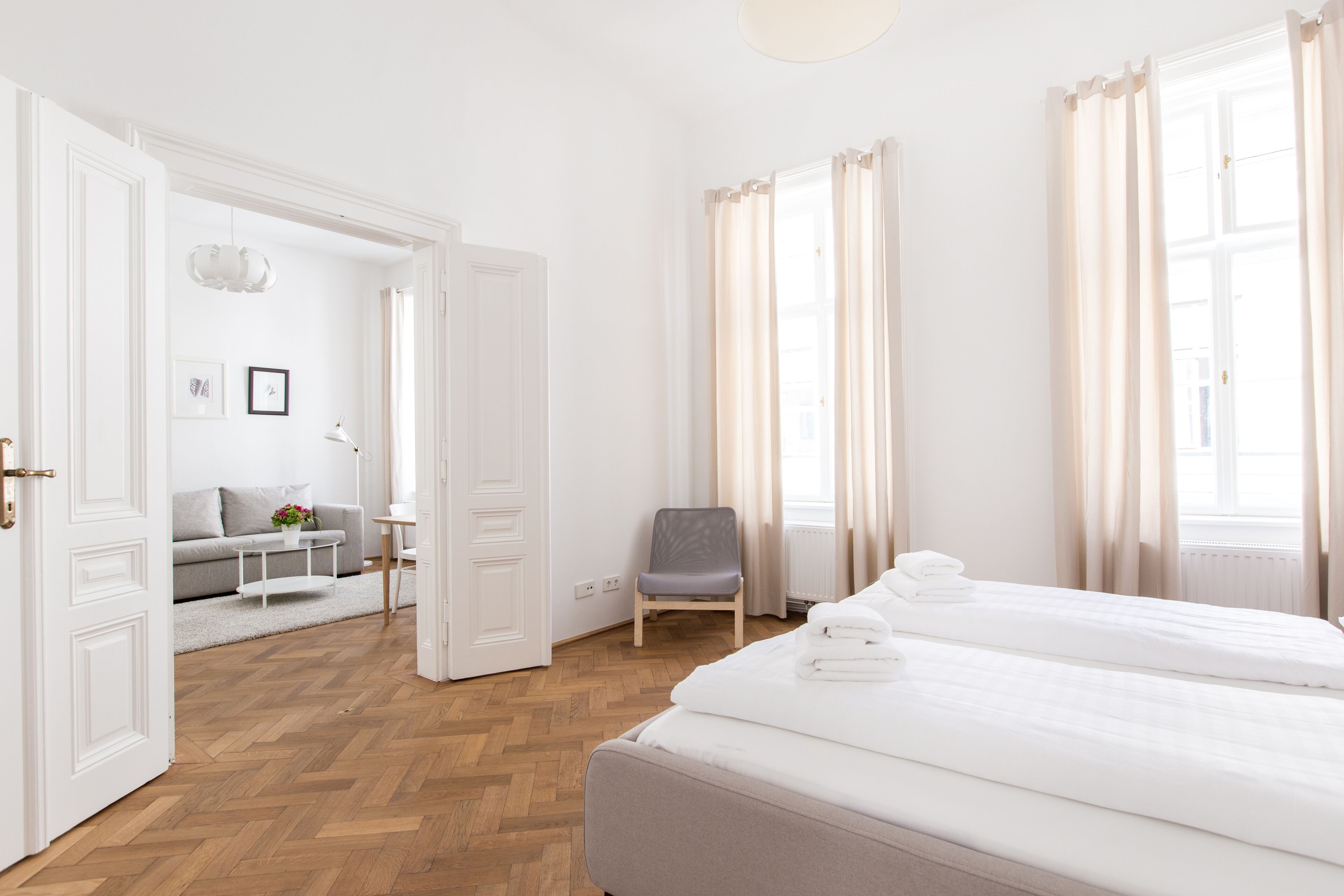 A hotel room with a double bed, a chair, a small table, and a sofa in the adjacent living area.