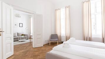 A hotel room with a double bed, a chair, a small table, and a sofa in the adjacent living area.
