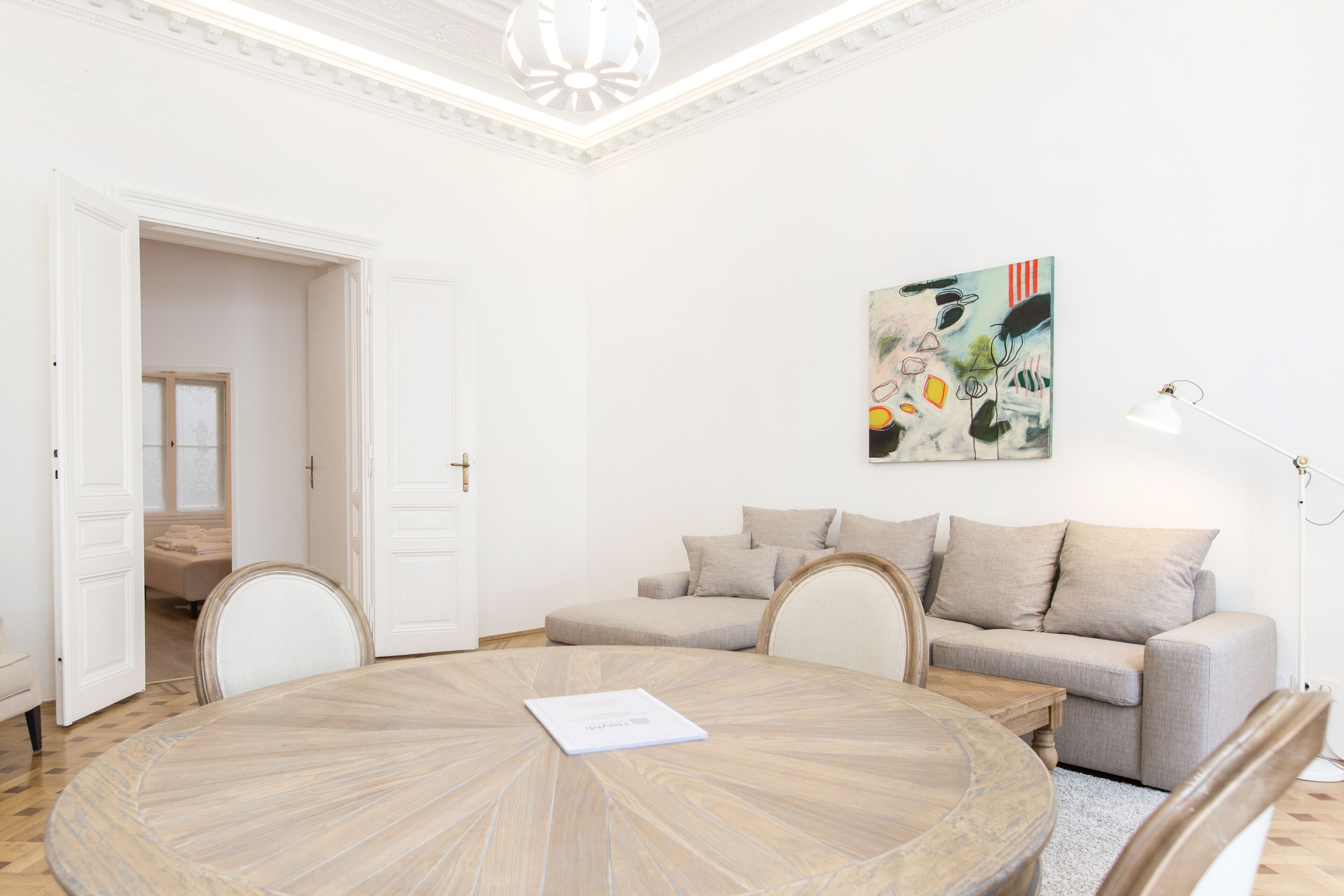 A room with a round wooden table, a beige sofa, and a painting on the wall.