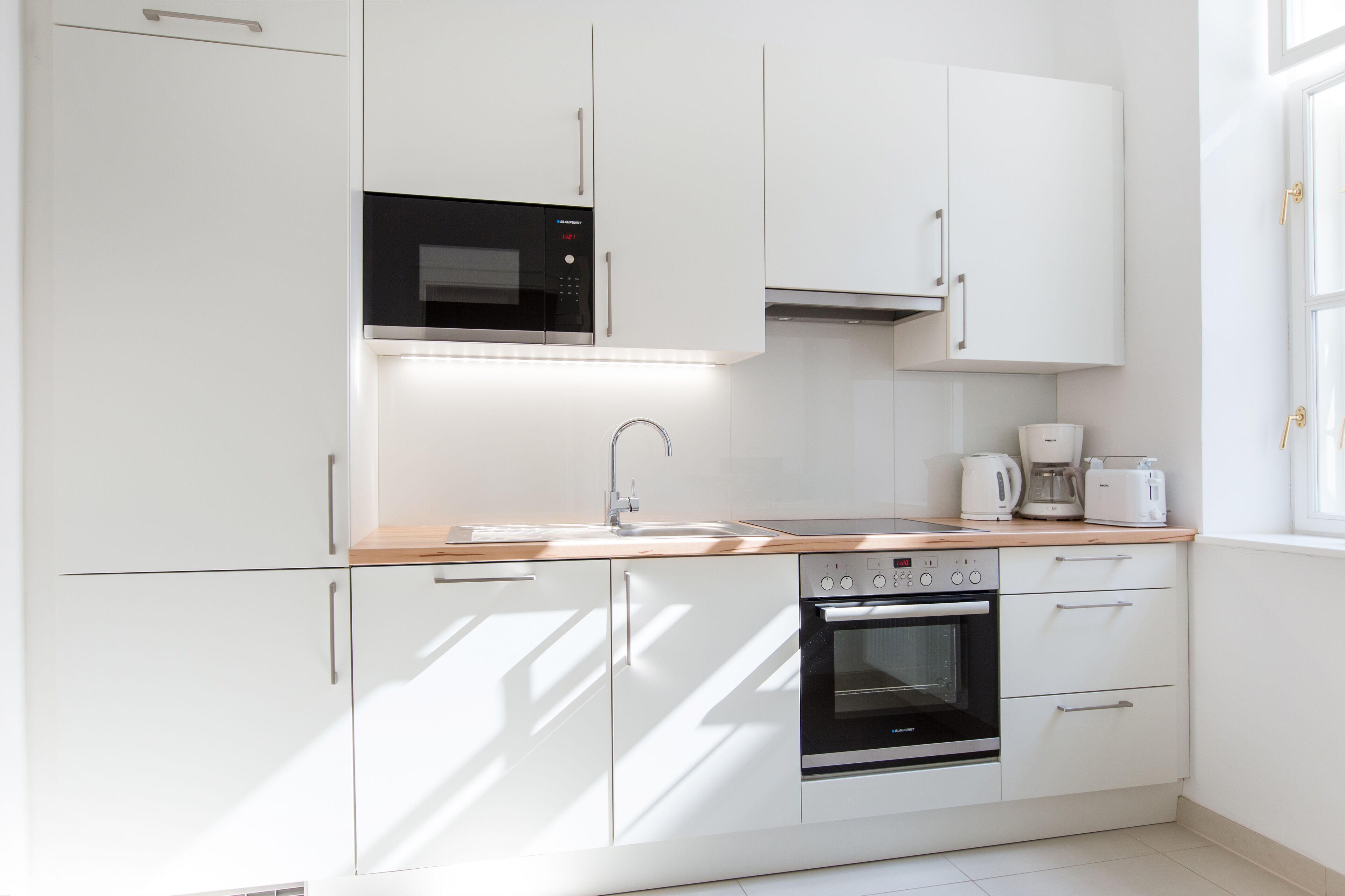 A modern kitchen with white cabinets, a microwave, a coffee maker, and an oven.