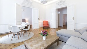 A spacious living room with a wooden coffee table, a grey sofa, and a white dining area with chairs. - HeyMi Apartments in City Center (Vienna)