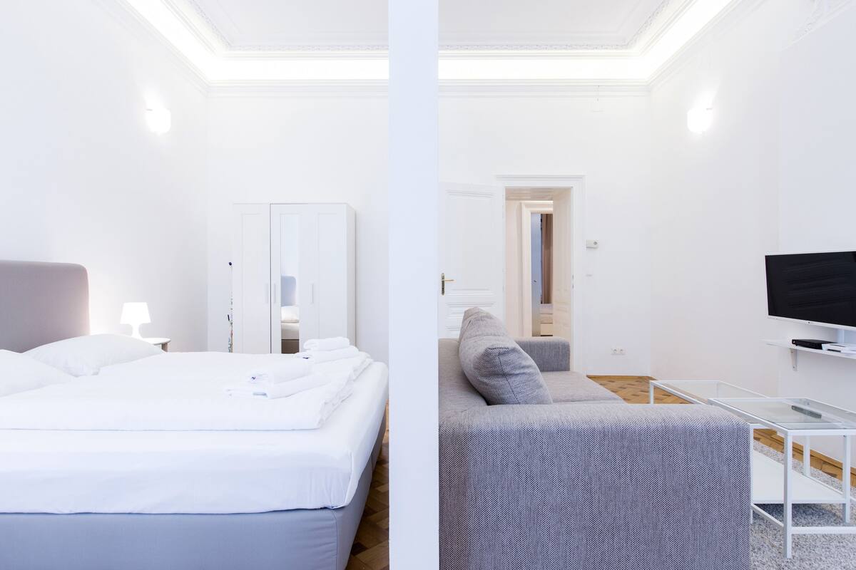 Moderni hotellihuone, jossa on sänky, sohva, televisio ja peili.