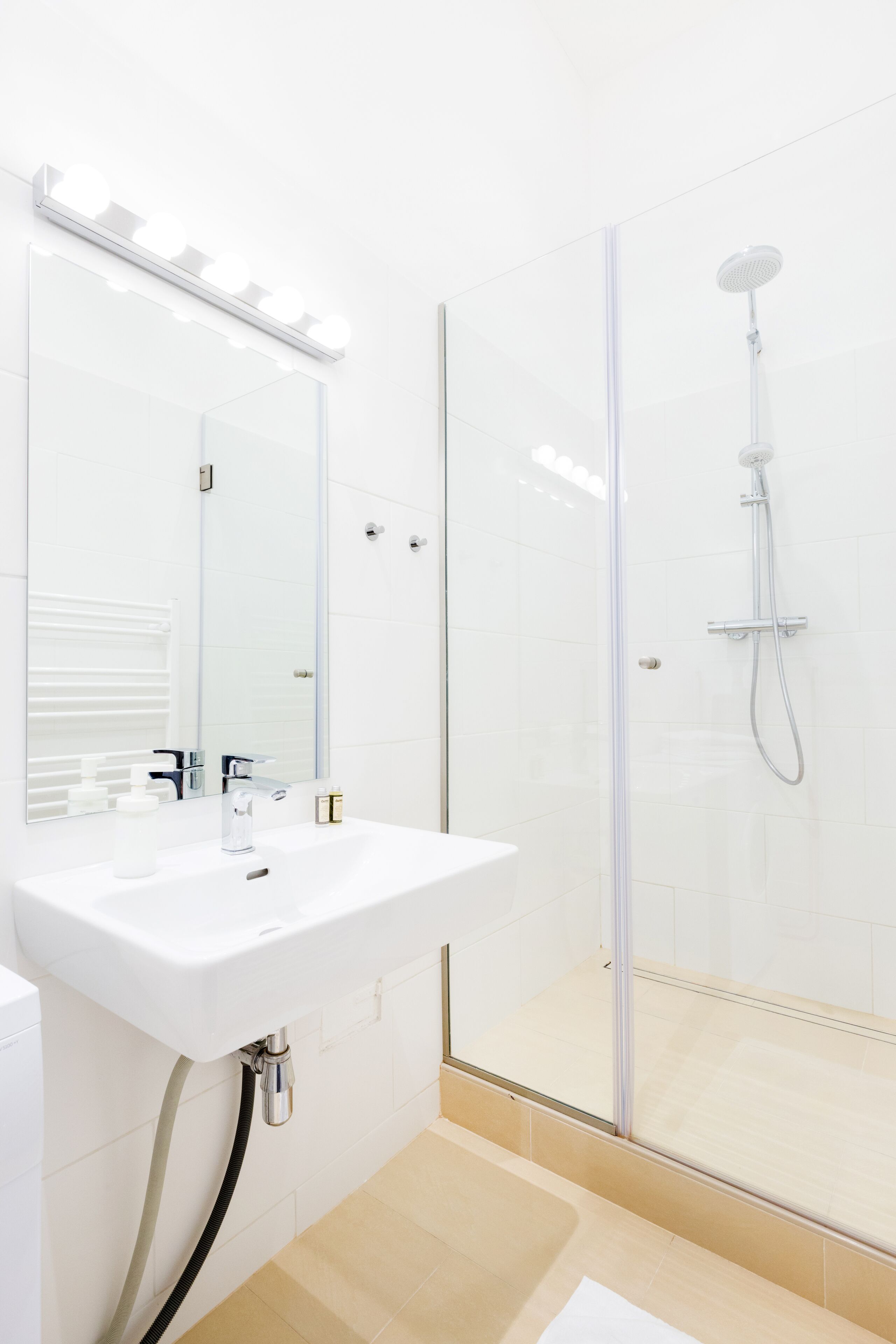 A modern bathroom with a glass-enclosed shower, a white sink, and a large mirror with lights above.