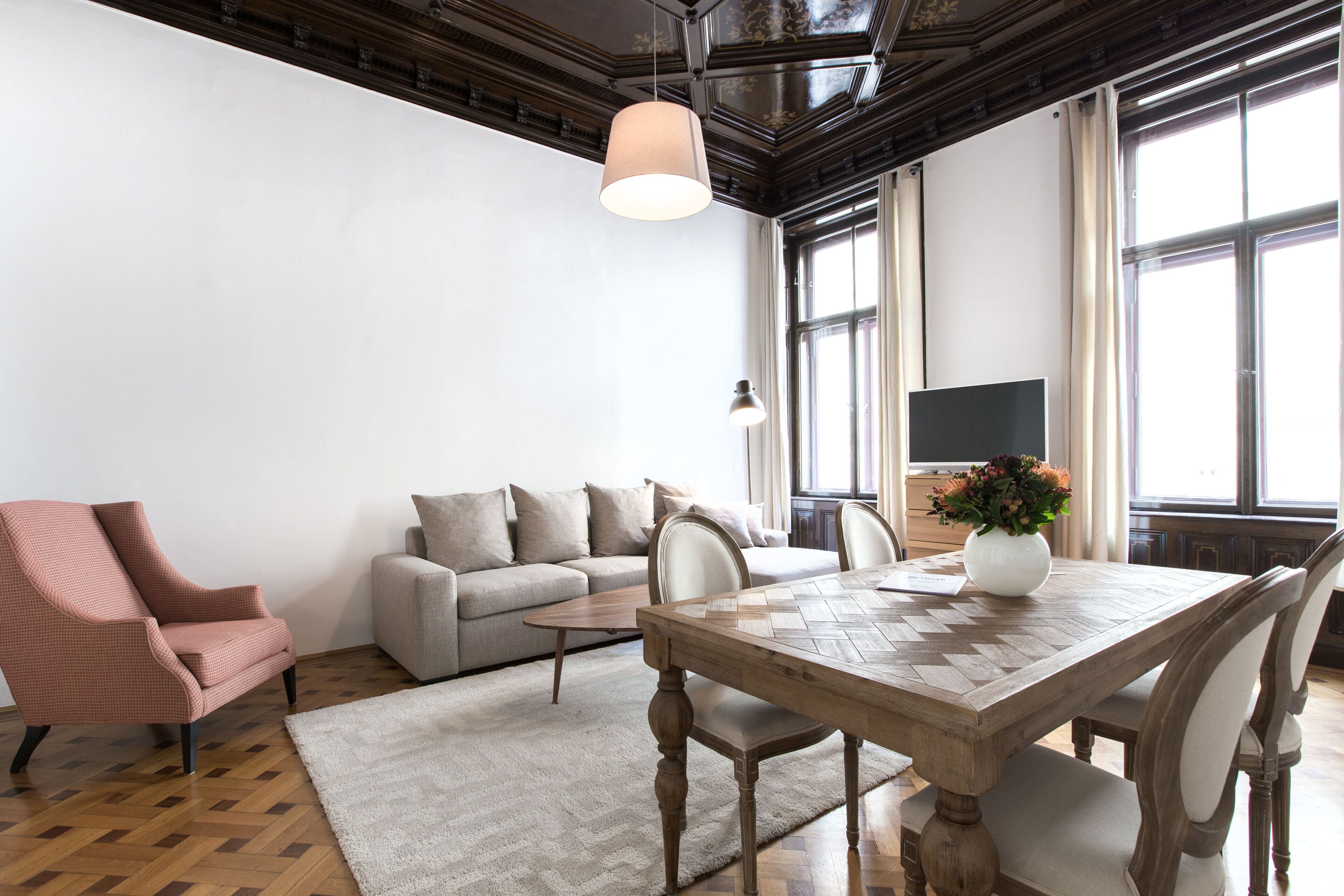 A spacious living room with a wooden dining table, a sofa, a chair, and a TV.