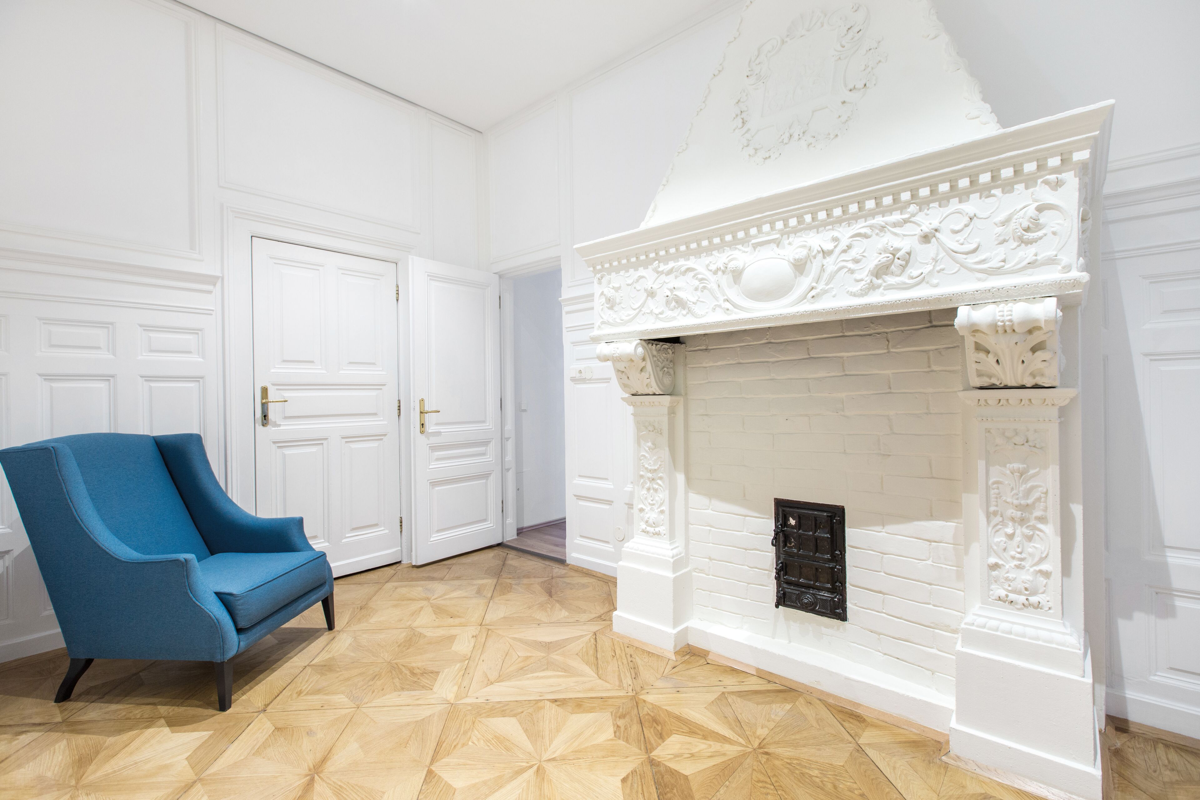 A room with a white fireplace, a blue armchair, and a patterned wooden floor.
