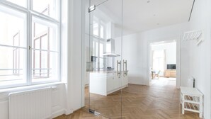 A modern kitchen with white cabinets, a glass partition, and a wooden herringbone floor. - HeyMi Apartments in City Center (Vienna)
