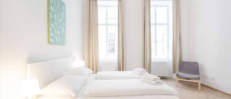 A modern hotel room with a large bed, two windows, a chair, and a hanging light fixture.