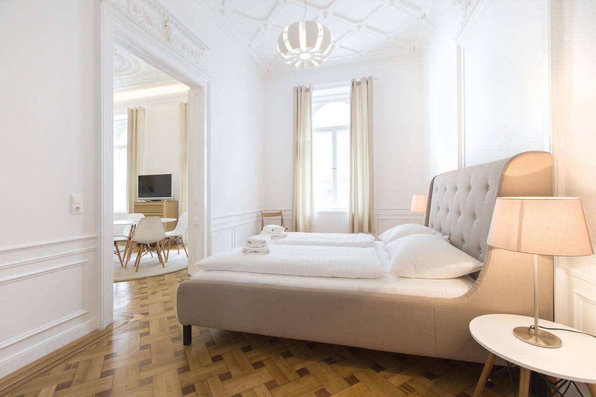 Hotellihuone, jossa on suuri sänky, yöpöytä, lamppu ja näkymä ruokailutilaan.