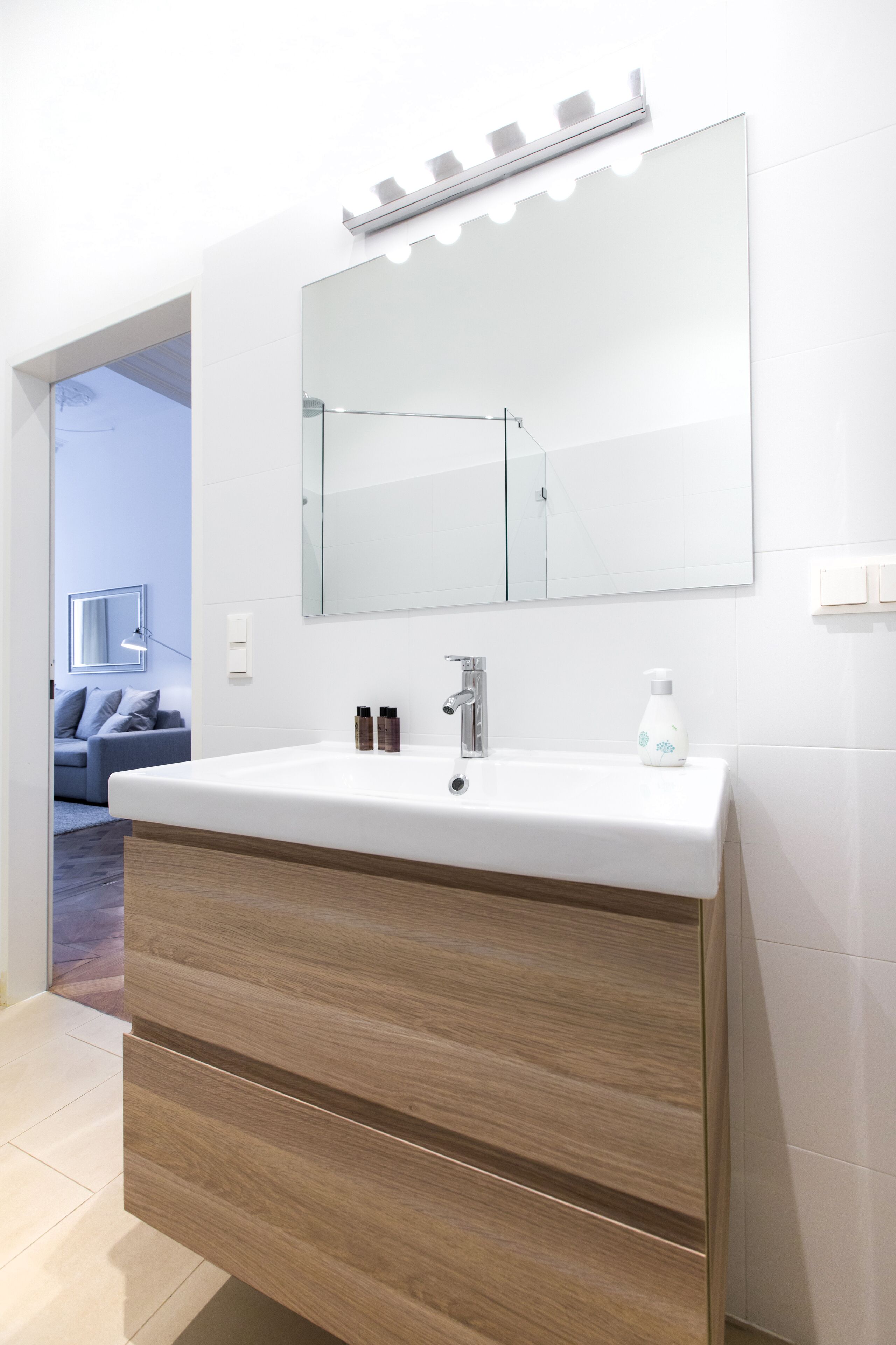 Een moderne badkamer met een witte wastafel, een houten opbergmeubel en een grote spiegel.