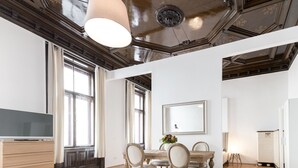 A spacious living room with a wooden dining table, comfortable seating, a large mirror, and a ceiling with intricate woodwork. - HeyMi Apartments in City Center (Vienna)