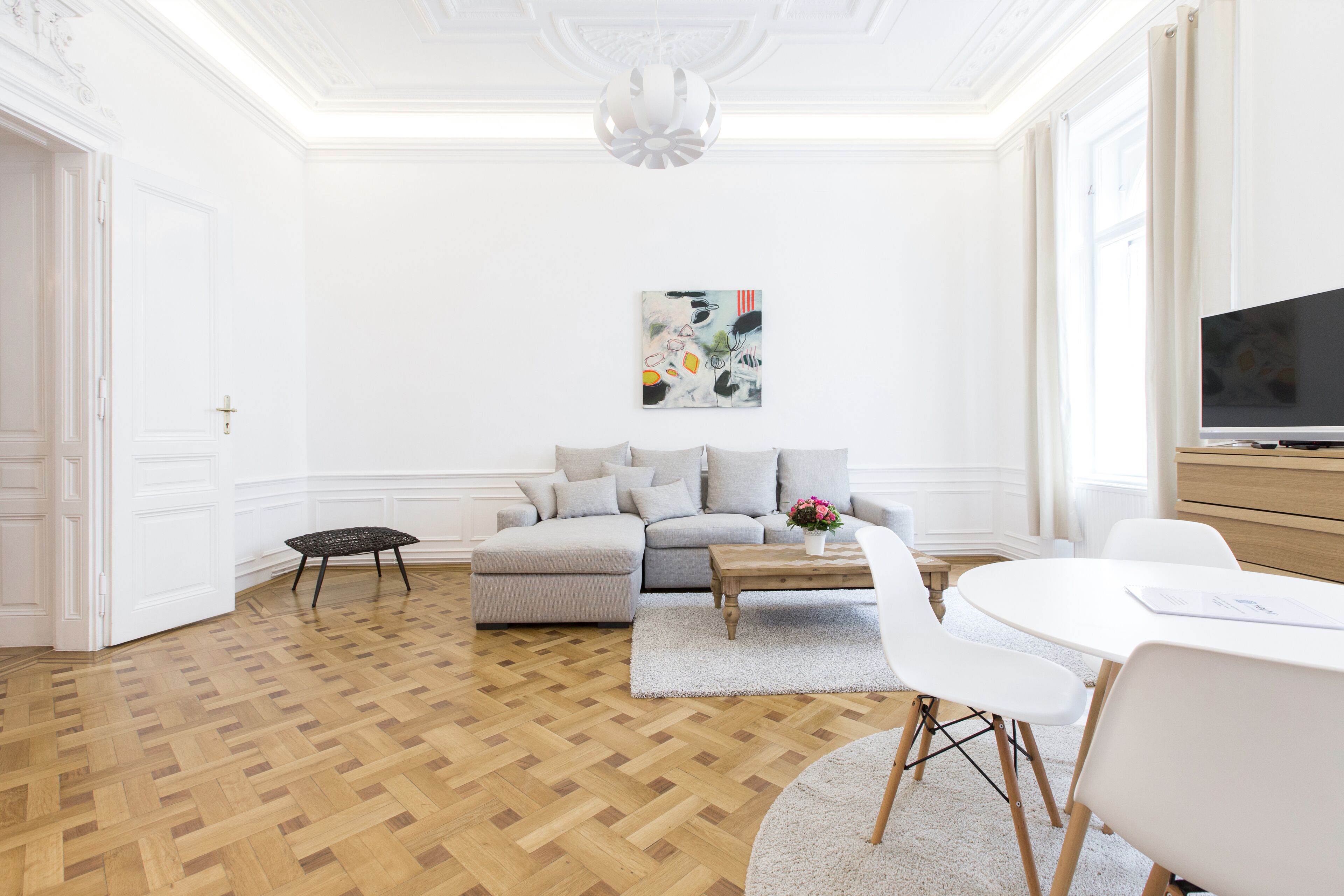 Un salon spacieux doté d’un parquet en bois, d’un canapé gris, d’une table basse blanche et d’un téléviseur posé sur un meuble en bois.